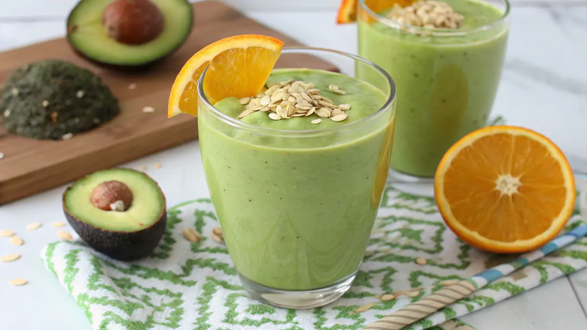 A green avocado oatmeal smoothie served in a glass, topped with a slice of orange and a sprinkle of oats.